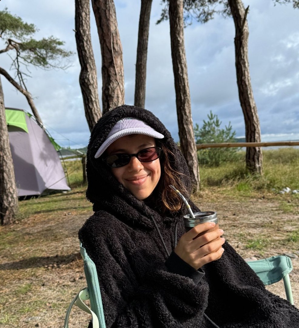 Mica sonriendo con un mate al aire libre, entre pinos